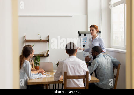 Female leader coach give presentation for diverse employees at meeting Stock Photo