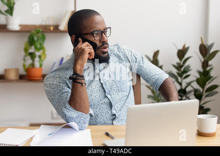 Serious african businessman talking on phone sitting at office desk Stock Photo