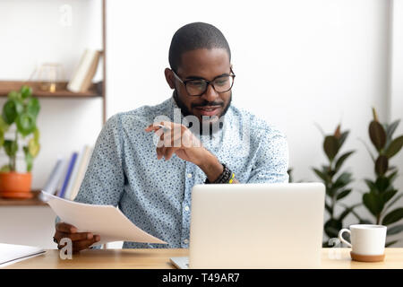 Focused african american businessman working with laptop documents in office Stock Photo