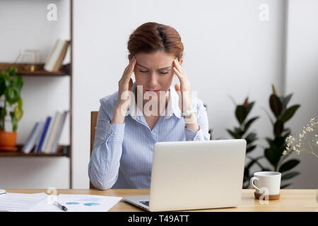 Tired frustrated businesswoman coping with strong headache attack at workplace Stock Photo