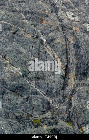 Weathered gray rock face with orange and white mineral veins as a nature background Stock Photo