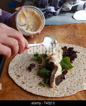 A woman making a vegetarian wrap on a wooden work top in a modern kitchen. Stock Photo