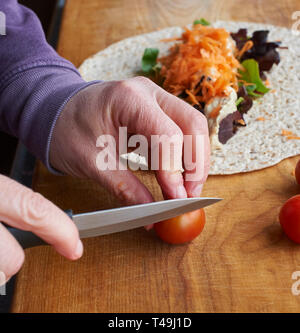 A woman making a vegetarian wrap on a wooden work top in a modern kitchen. Stock Photo