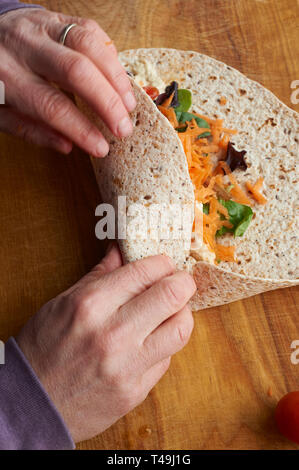 A woman making a vegetarian wrap on a wooden work top in a modern kitchen. Stock Photo