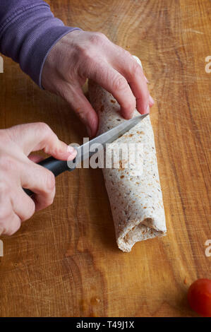 A woman making a vegetarian wrap on a wooden work top in a modern kitchen. Stock Photo