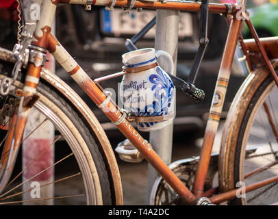 15 April 2019, Hessen, Frankfurt/Main: The owner of this bicycle, which is attached to a traffic sign and carries a pitcher in its drink holder, apparently has the bottle of wine with it at all times - the traditional container for pouring Frankfurt apple wine. Photo: Frank Rumpenhorst/dpa Stock Photo