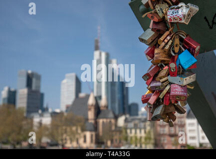 15 April 2019, Hessen, Frankfurt/Main: Numerous so-called 'castles of love' hang on the Iron Bridge, while the bank skyline can be seen in the background. The weather will also be sunny in the coming days. Photo: Lukas Görlach/dpa Stock Photo