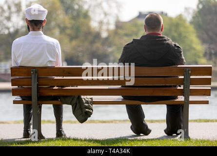 15 April 2019, Hessen, Frankfurt/Main: Two men sit on a bench on the banks of the Main river in the sun. One of the two wears a Muslim headgear on that occasion. The weather is expected to show its spring-like side in the coming days. Photo: Lukas Görlach/dpa Stock Photo