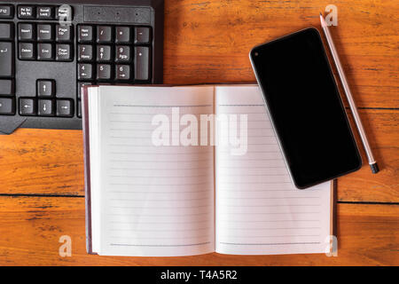 Notebook keyboard and smart phone on wooden table background. Stock Photo