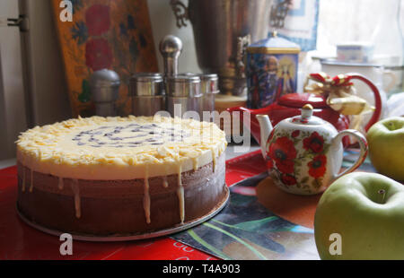 Homemade sweet chocolate cake near painted teapots, green apples and a samovar on the table Stock Photo