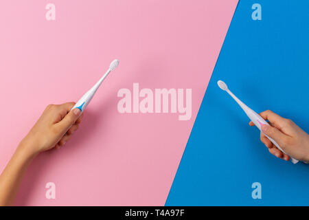 Kid hands with electric toothbrushes on pink and blue background. Stock Photo