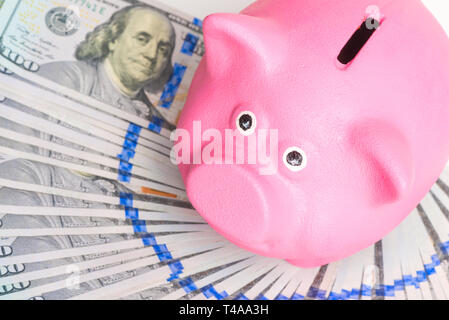 pink piggy bank stands on a fan of a pile of american dollars on a white background top view
