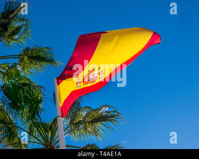 Spanish Flag undulating and unfurling in a sea breeze on flagpole with palm trees behind at San Pedro de Alcantara Malaga Costa del Sol Spain Stock Photo