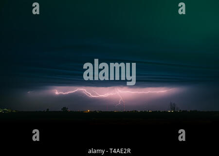 View of lightning strike over a rural farm field, lightning strikes the ground, strong thunder, dark clouds in the sky in the Midwest. Stock Photo
