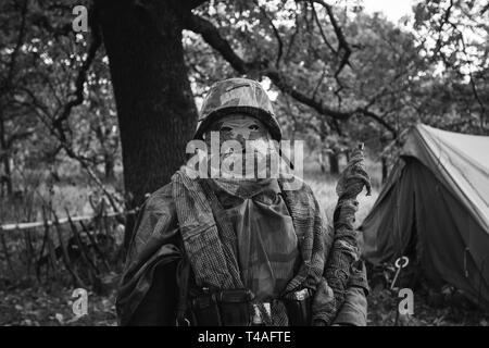 Hidden Re-enactor Dressed As World War Ii German Wehrmacht Sniper Soldier In Forest. Close Portrait In Camouflage.  Photo In Black And White Colors. Stock Photo