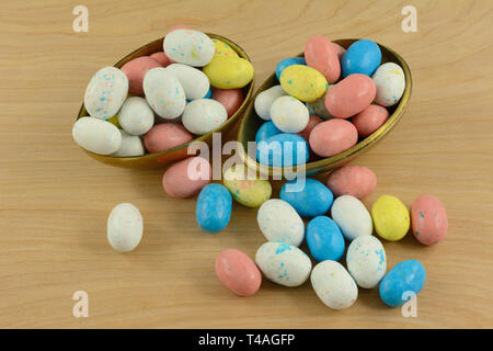 Candy covered malted milk chocolate for Easter in shape of bird eggs spilling out of brass Easter egg halves on wooden table Stock Photo