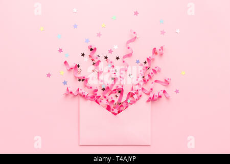 Confetti and pastel stars explosion. Envelope with festive streamers on pink. Party invitation concept. Flat lay, minimal style. Stock Photo