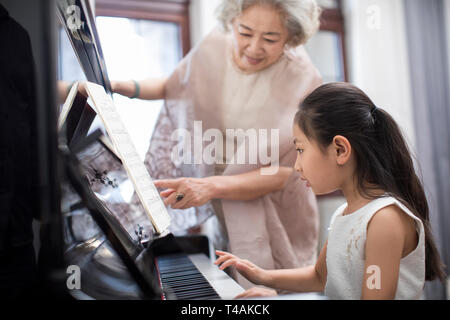 Grandmother teaching granddaughter to play the piano Stock Photo