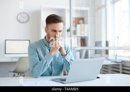 Pensive Young Man Using Laptop Stock Photo