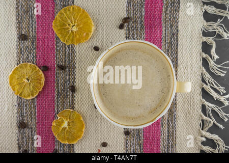 A Cup of coffee in a cozy style on a striped fabric background. Slices of dried orange and coffee beans. Flat lay. Stock Photo
