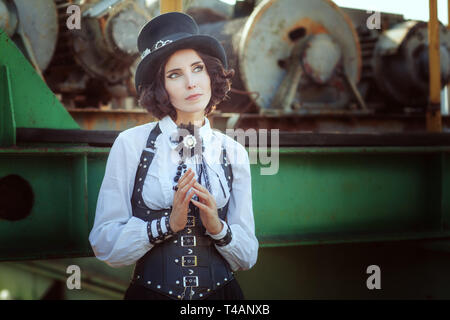 Beautiful young girl dressed in the style of steampunk looks thoughtfully at the sky. Stock Photo