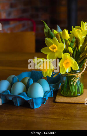 Blue Eggs and Yellow Daffodils on a Wooden Table in Springtime Stock Photo