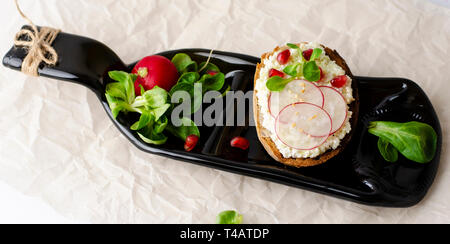 Toasts with cottage cheese and smashed avocado, radish, corn salad plant and pomegranate seeds on a serving bottle-plate. Top view. Copy space. Health Stock Photo