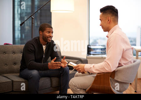 Man Sitting On Couch Meeting With Male Counsellor In Office Stock Photo