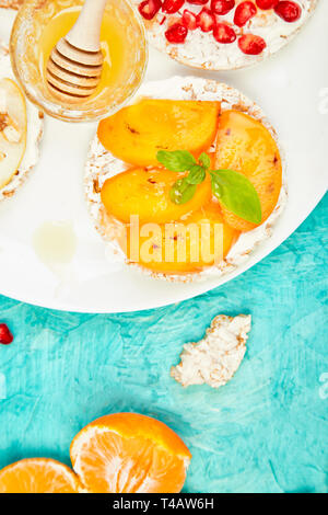 Rice Crisp bread healthy snack with tropical fruit - pomegranate, tangerine, persimmon, apple. Easy breakfast close-up on a blue background. Summer ve Stock Photo