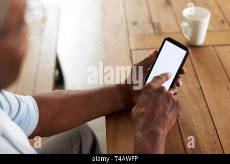 Senior black man sitting at a table using smartphone, over shoulder view Stock Photo