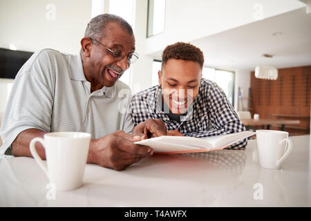 Young black man looking at a photo album at home with his grandfather, close up Stock Photo