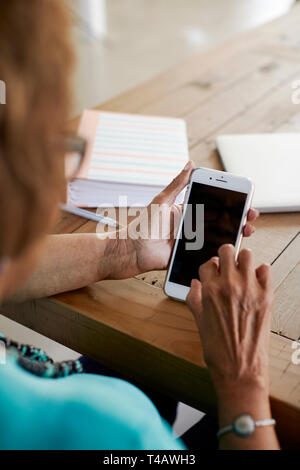 Over shoulder view of senior black woman sitting at table using smartphone, close up, vertical Stock Photo