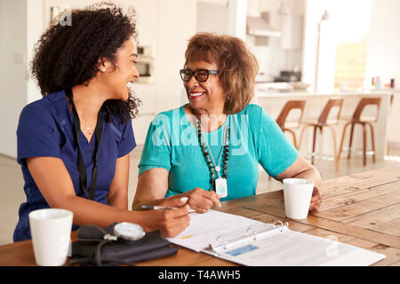 Female healthcare worker sitting at table smiling with a senior woman during a home health visit Stock Photo