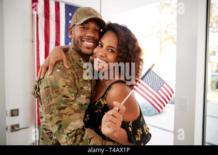 Millennial black soldier and wife embracing at home and smiling to camera,waving flag, close up Stock Photo
