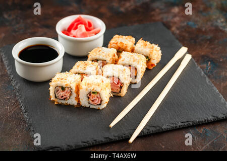 Japanese sushi rolls served on stone slate on dark background. Sushi rolls, maki, pickled ginger and soy sauce. Sushi background. Asian or Japanese fo Stock Photo