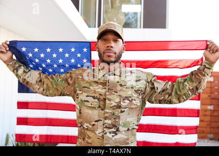 Millennial black soldier standing outside modern building holding US flag, looking to camera, close up Stock Photo