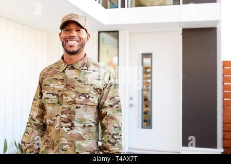 Millennial soldier in camouflage uniform standing outside modern house smiling to camera, close up Stock Photo