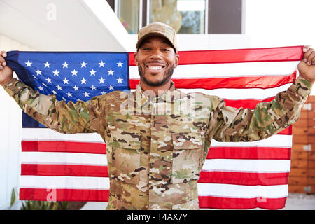 Millennial black soldier standing outside modern building holding US flag, smiling to camera, close up Stock Photo