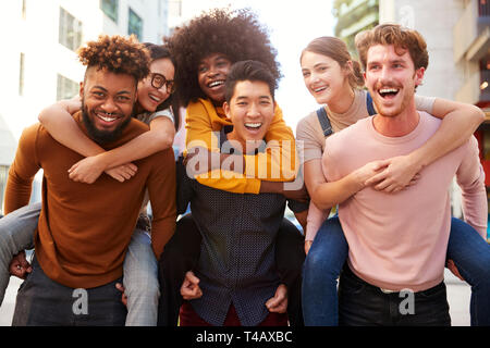 Three young adult couples having fun piggybacking in a city street, close up Stock Photo
