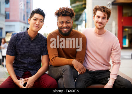 Three millennial male hipster friends on a bench in a city street smiling to camera, close up Stock Photo