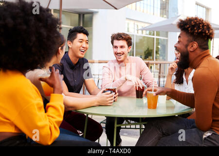 Six trendy millennial friends drinking cold brews and talking, sitting in the street outside a cafe Stock Photo