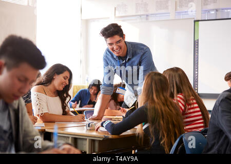 Male High School Teacher Standing By Student Table Teaching Lesson Stock Photo