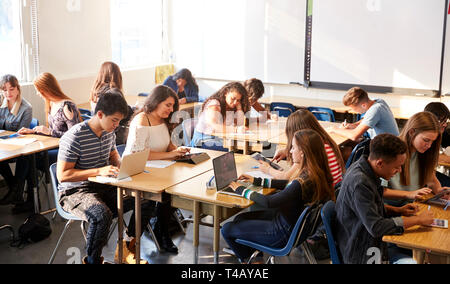 Wide Angle View Of High School Students Sitting At Desks In Classroom Using Laptops Stock Photo