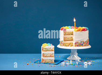 Sliced confetti Birthday cake  with lit candle, colorful icing and Sprinkles over a blue background. Stock Photo