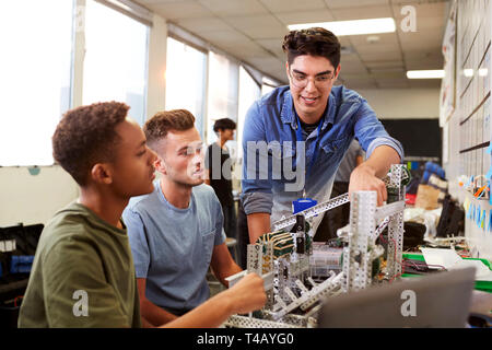 Teacher With Two Male University Students Building Machine In Science Robotics Or Engineering Class Stock Photo