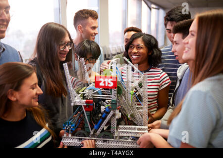 College Students With Teacher Holding Machine In Science Or Robotics Class Stock Photo