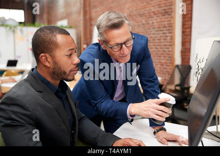 Two Businessmen Working At Computer On Desk In Open Plan Office Stock Photo