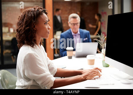 Mature Businessman Working At Table On Laptop In Open Plan Office With Colleagues In Background Stock Photo