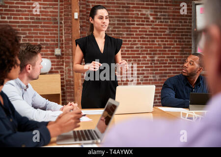 Young Businesswoman Standing And Leading Office Meeting Around Table Stock Photo
