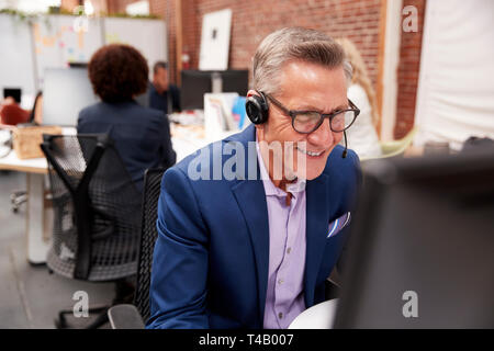 Mature Male Customer Services Agent Working At Desk In Call Center Stock Photo
